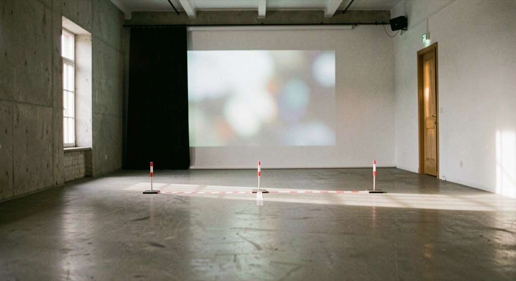 Una sala d’assaig buida amb llum lateral, cinta de marcatge i una projecció difusa al fons